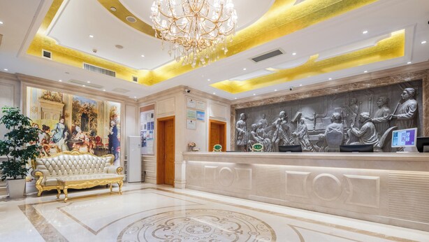 Un vestíbulo con candelabro, mostrador de recepción y un mural.
