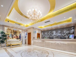 Un vestíbulo con candelabro, mostrador de recepción y un mural.