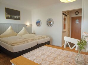 Un dormitori amb un llit, una tauleta de nit, un mirall penjat a la paret i una porta que condueix a una altra habitació.