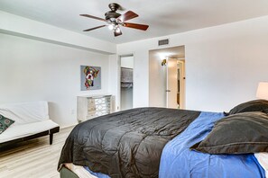 A bedroom with a bed, a ceiling fan, a painting, and a wardrobe.
