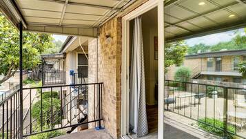 A residential balcony with a metal railing, a staircase leading to an upper level, and a view of neighboring houses.