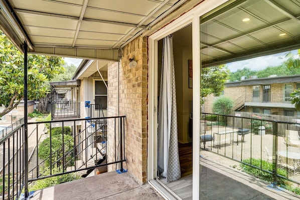 A residential balcony with a metal railing, a staircase leading to an upper level, and a view of neighboring houses.