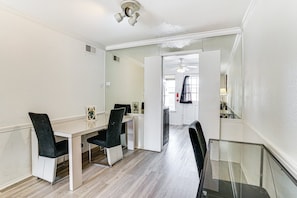 A hotel room with a dining area featuring a white table, black chairs, and a glass-top table.