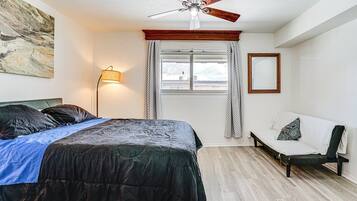 A bedroom with a bed, a chair, a ceiling fan, a window with curtains, and a lamp.