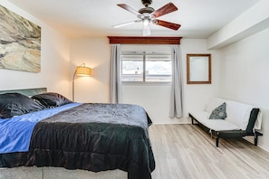 A bedroom with a bed, a chair, a ceiling fan, a window with curtains, and a lamp.