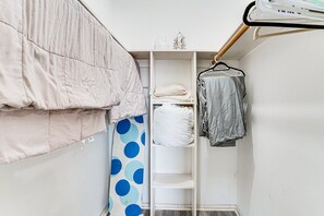 Een slaapkamer met een bed, een plank met opgevouwen kleding en een kapstok met een handdoek.