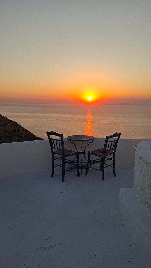 A table and two chairs on a terrace overlooking a sunset over the sea.