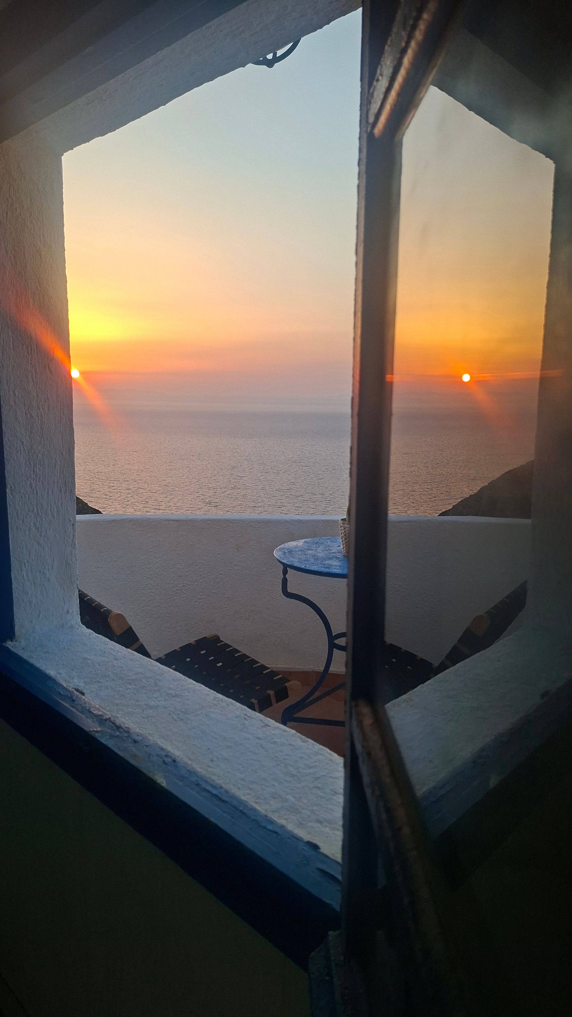 Une vue depuis une fenêtre donnant sur une étendue d’eau au coucher du soleil.