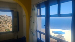 A room with a view of the sea and a table outside.