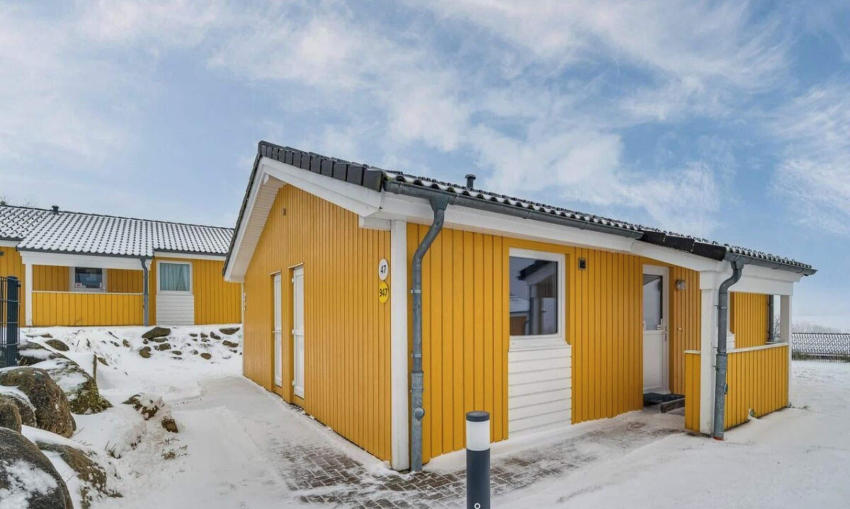 A yellow building with a white door and window, surrounded by snow.
