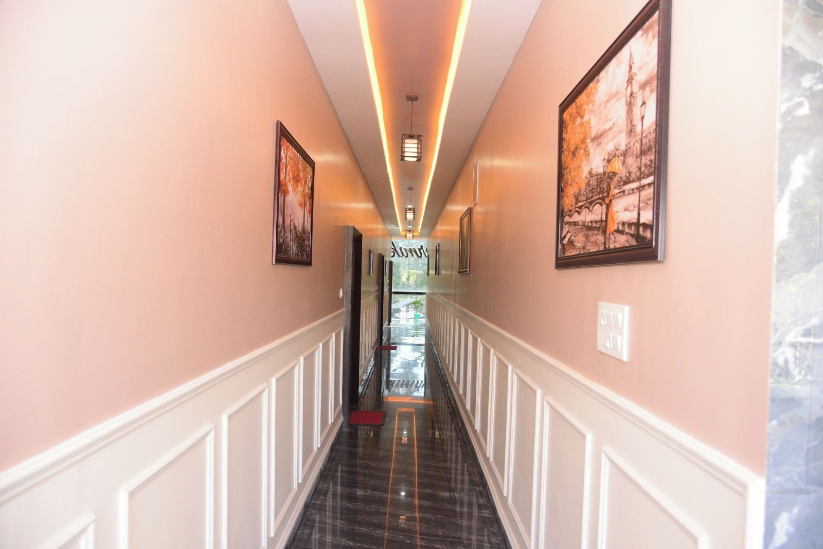 A hotel corridor with a marble floor, white wainscoting, and framed artwork on the walls.