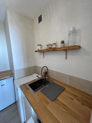 A kitchen with a built-in sink, wooden countertop, and a small refrigerator. - Escapade Iodée • Cocon Calme & Télétravail (Saint-Hilaire-de-Riez)
