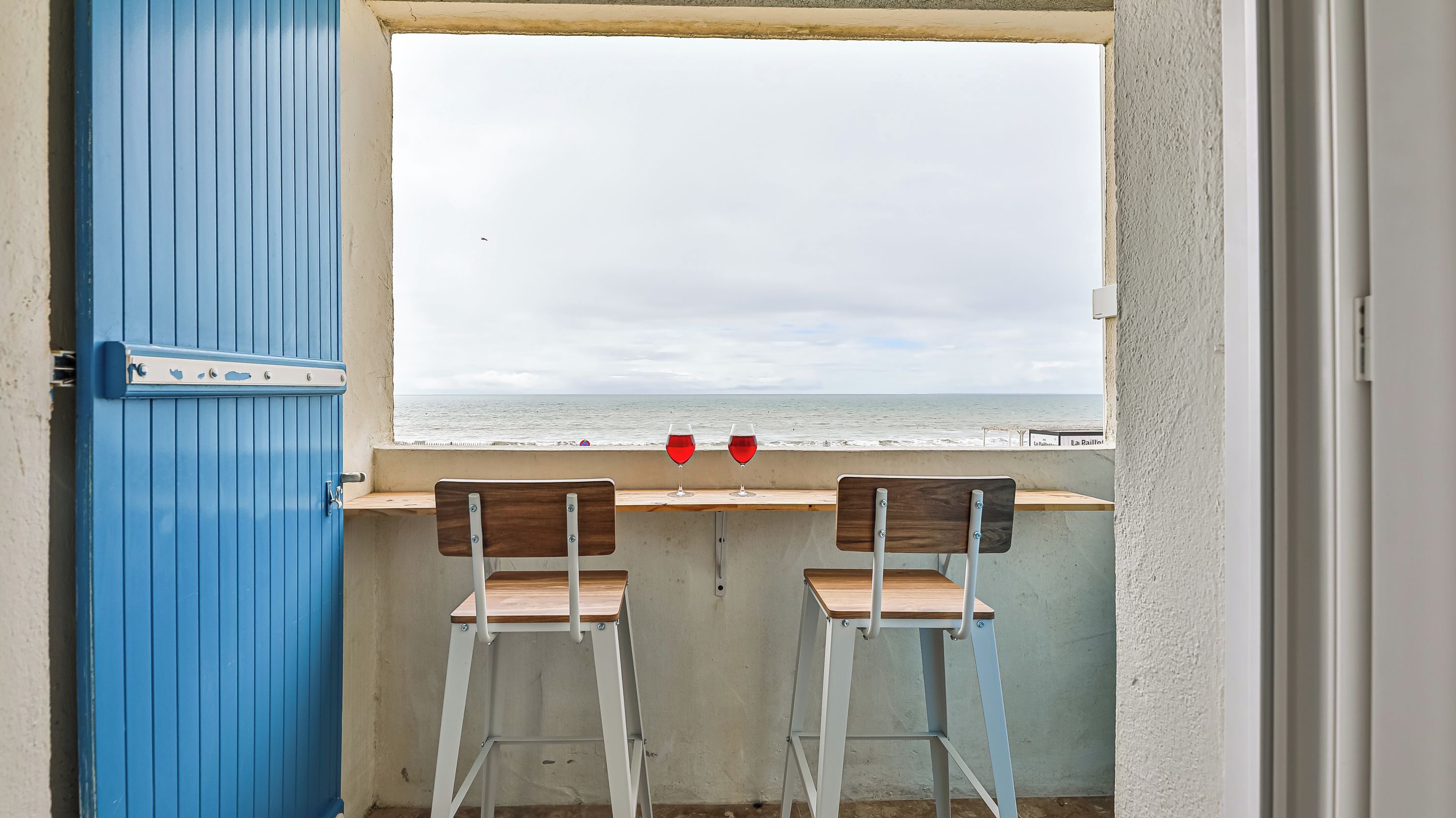 Een balkon met twee houten stoelen en een tafel, met uitzicht op de zee.