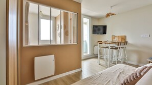 Ein modernes Zimmer mit einem Bett, einem Schreibtisch mit Stühlen, einem Fernseher und einem Fenster mit Vorhängen.