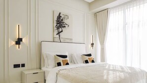Quarto de hotel com uma cama grande, mesas de cabeceira, uma obra de arte na parede e uma janela com cortinas.