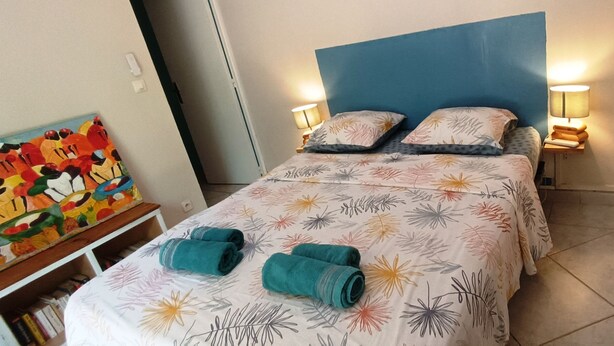 Una camera d'albergo con un letto, due abat-jour, un quadro appeso e uno scaffale con libri.