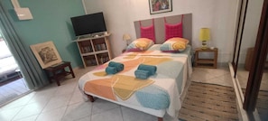A bedroom with a bed, a TV, a bookshelf, and a bedside lamp. - Vrbo Property (Les Trois-Îlets)