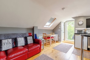 A modern loft with a red leather sofa, a dining area, a kitchenette, and a skylight. - Viewpoint Studio | Shropshire Countryside Stay (Stretton Westwood)