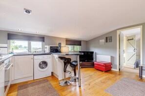 A compact kitchen with a washing machine, a dining area with a bar stool, a red ottoman, and a television. - Viewpoint Studio | Shropshire Countryside Stay (Stretton Westwood)