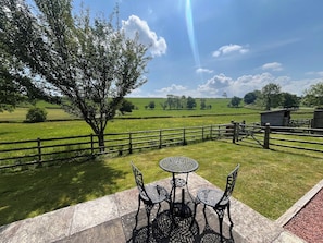 A patio with a table and chairs, a wooden fence, and a tree in a rural setting. - Viewpoint Studio | Shropshire Countryside Stay (Stretton Westwood)