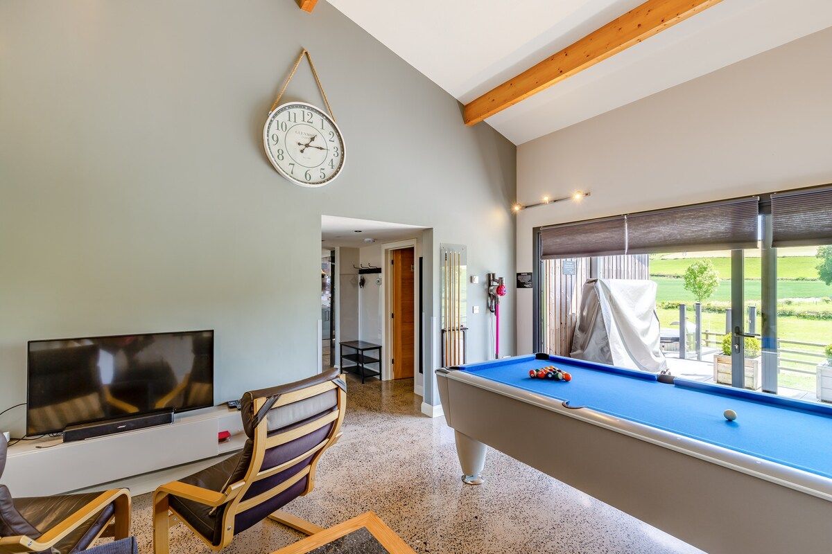 A room with a pool table, a television, and a clock on the wall.