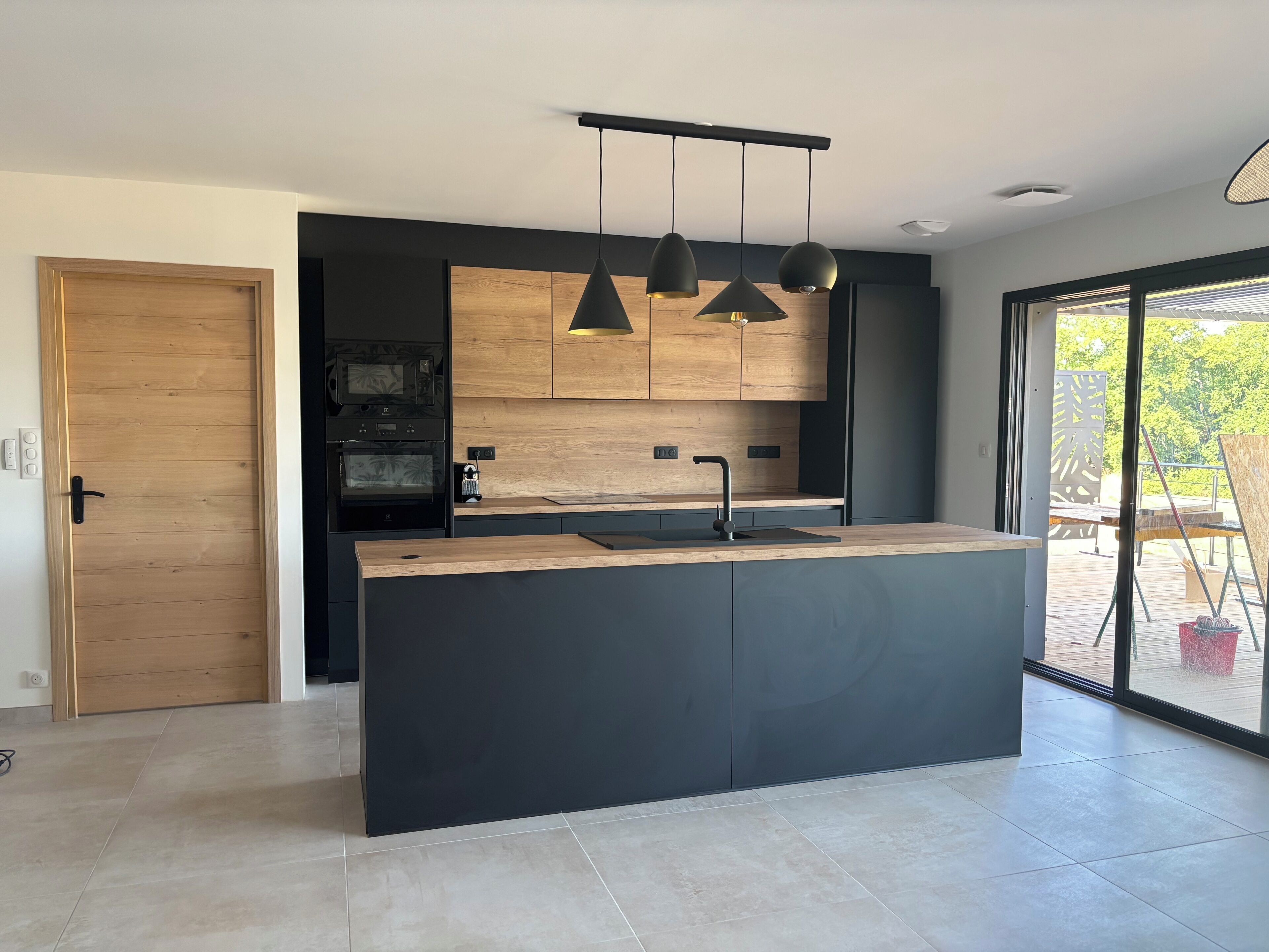 Une cuisine moderne dotée d’un îlot central, de luminaires suspendus et offrant une vue sur l’extérieur.