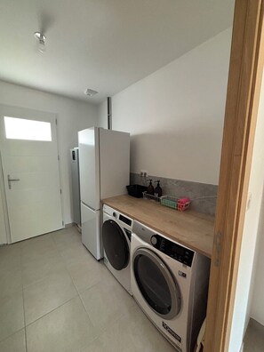 A compact laundry room with a washing machine, dryer, and a small countertop with bottles and containers. - Charming vacation rental (Cublac)
