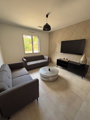 A living room with a sofa, a coffee table, a TV mounted on the wall, and a ceiling fan. - Charming vacation rental (Cublac)