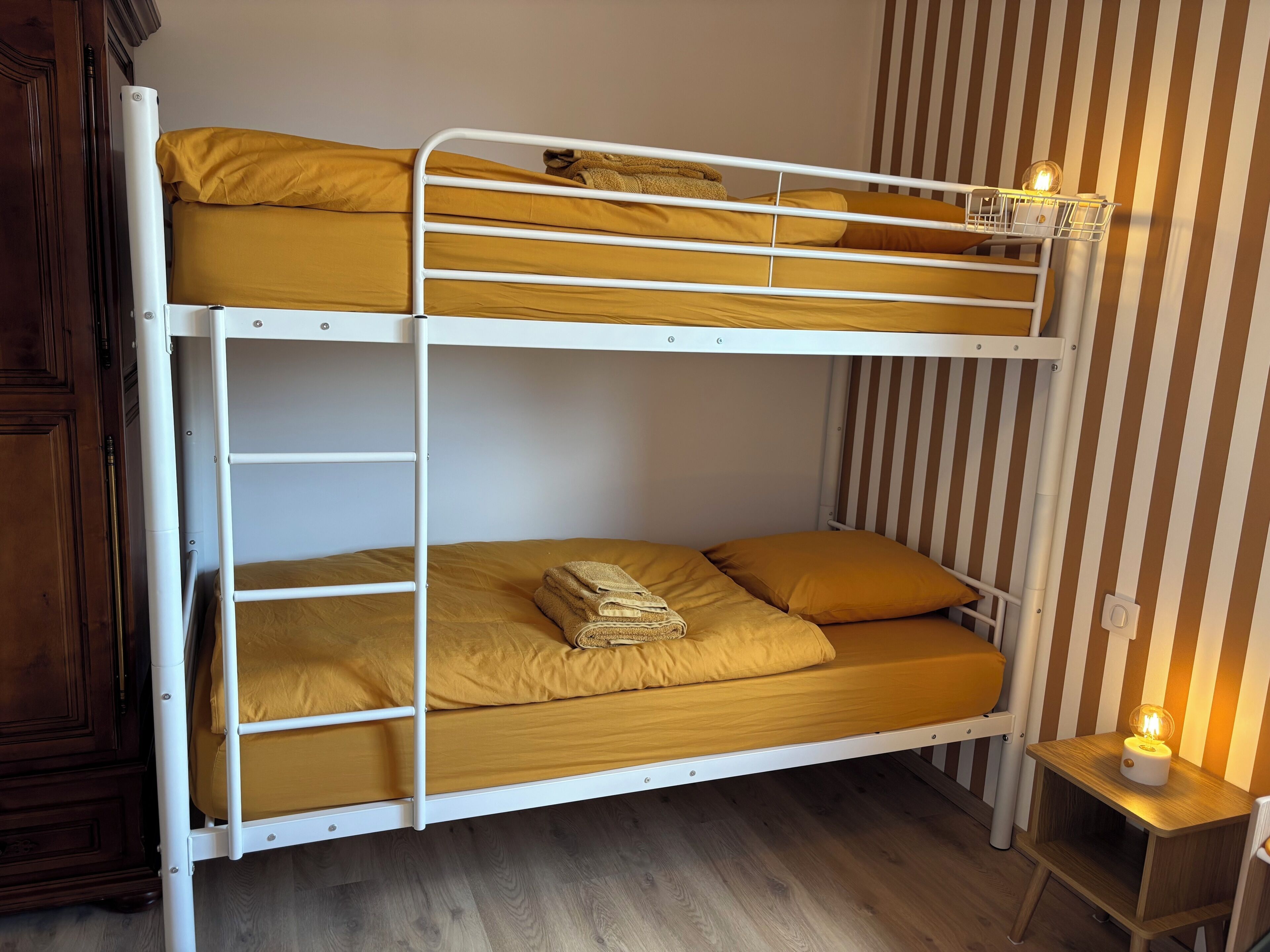 Een stapelbed met twee verhogingen, een houten kast, een gestreepte wand en een klein nachtkastje met een lampje.