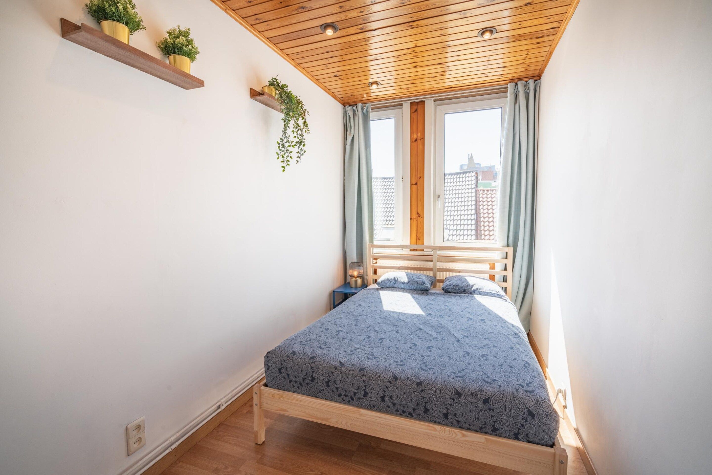 Un dormitorio con techo de madera, una cama con colcha estampada, dos mesitas de noche y una ventana con cortinas.