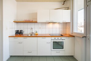 Cocina compacta con armarios blancos, pileta de acero inoxidable, horno integrado y ventana que proporciona luz natural.