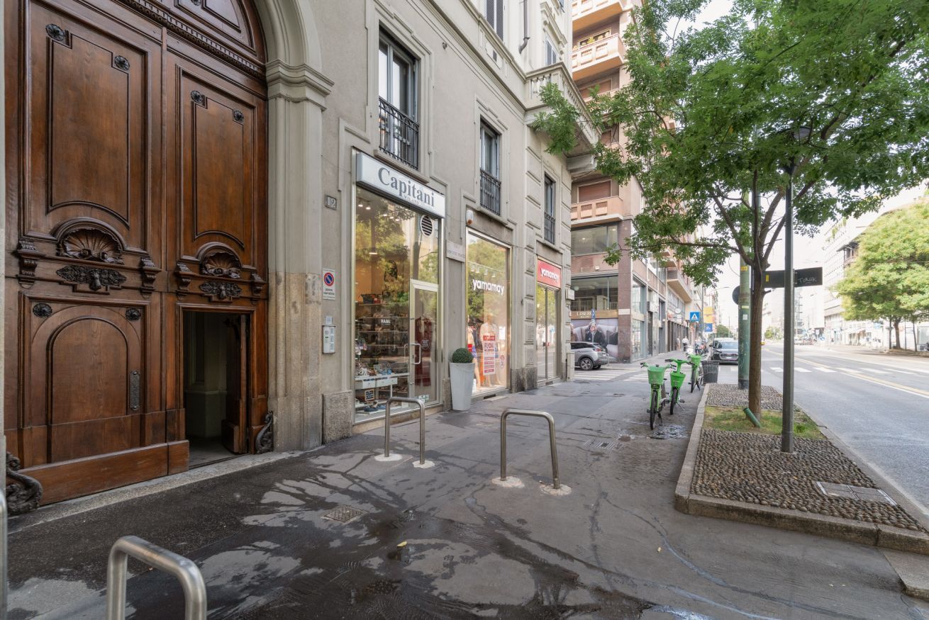 Une vue de rue avec la façade d’un bâtiment en bois, une devanture de magasin portant l’inscription « Capitani », et un arbre sur le trottoir.