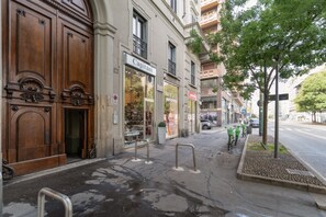 A street view with a wooden building facade, a storefront with a sign reading 'Capitani,' and a tree on the sidewalk. - A comfortable 65 sqm flat that sleeps up to 4 people, located on the 4th floor of a building with an elevator (though there are stairs to reach the entrance).The property is situated in the Piazza Cinque Giornate-Corso XXII Marzo area, a well served resi (Milan)