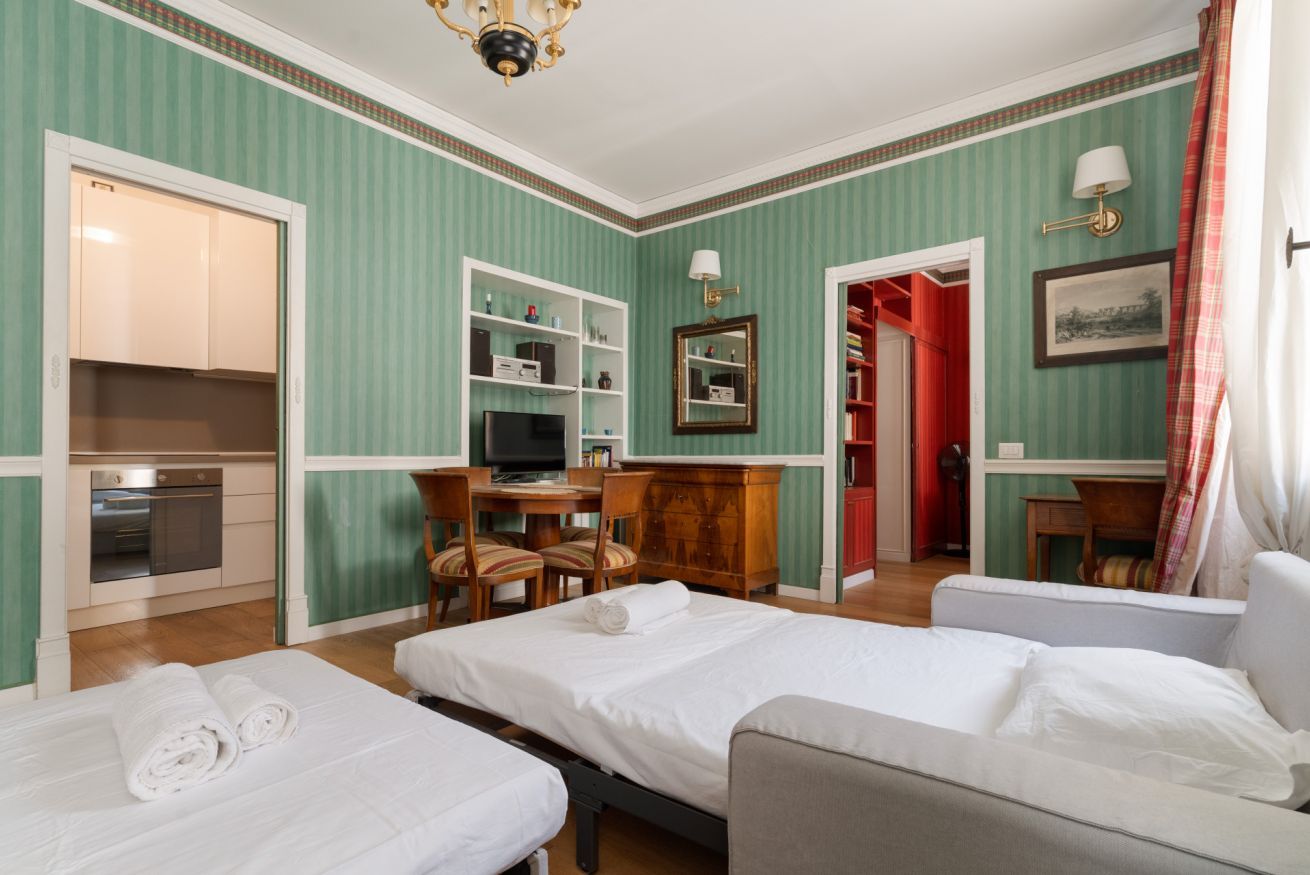 Habitación de hotel con dos camas, un escritorio con computadora, televisión, espejo y armario.