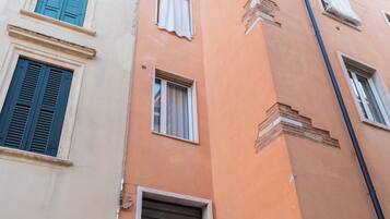 Ein mehrgeschossiges Gebäude mit einer Mischung verschiedener Fensterformen und Fensterläden, einschließlich eines Balkons mit Metallgeländer.