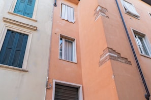Un edificio de varios pisos con una variedad de estilos de ventanas y contraventanas, incluyendo un balcón con barandilla de metal.