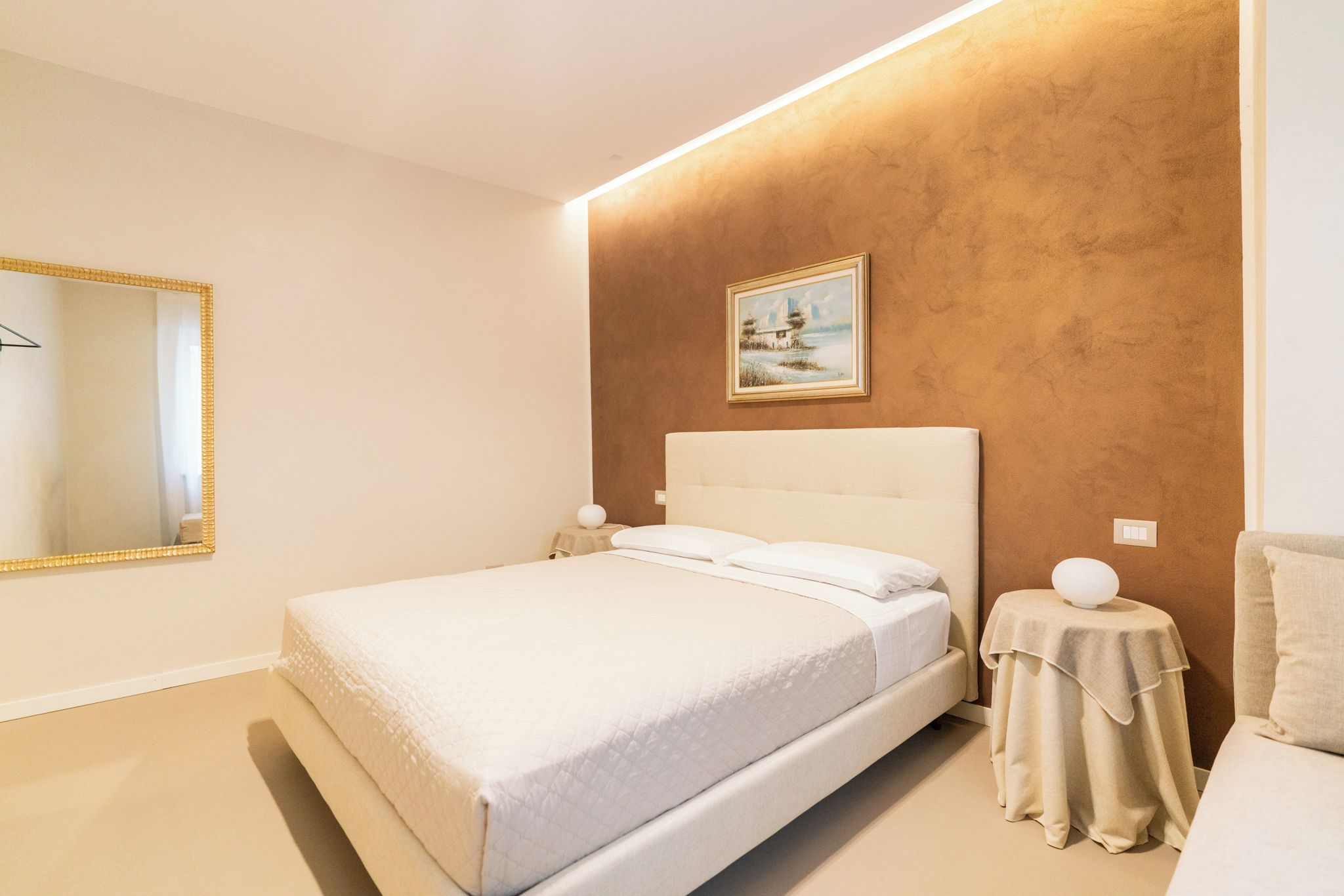 Un dormitorio con una cama, una mesita de noche, un espejo y un cuadro en la pared.