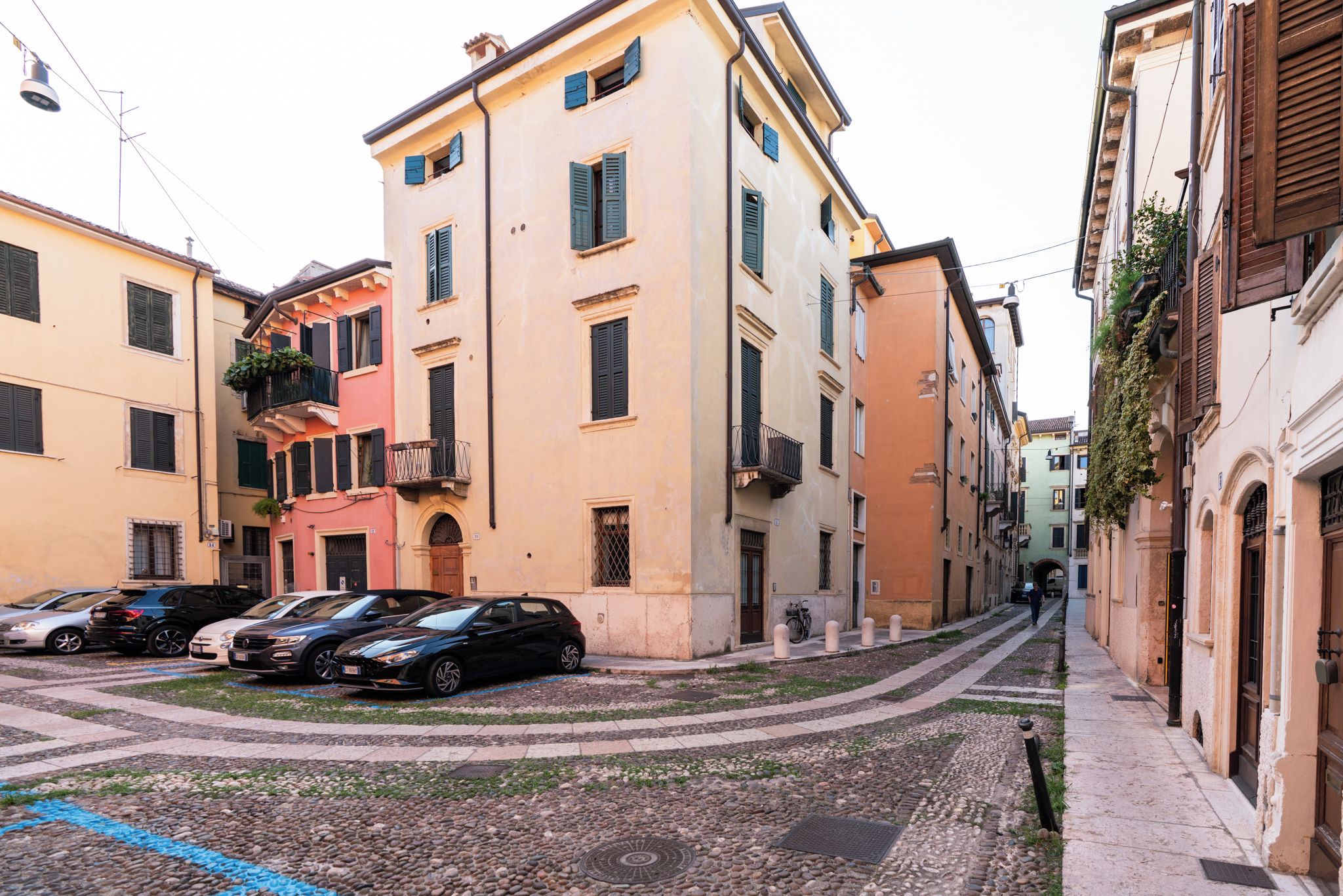 Una calle estrecha con coches aparcados y edificios con balcones.