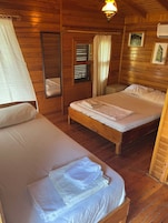 A wooden cabin room with two beds, a mirror, a window with blinds, and a picture on the wall.