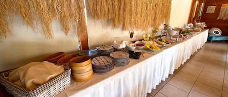 A buffet table with various food items and a woven wall hanging.