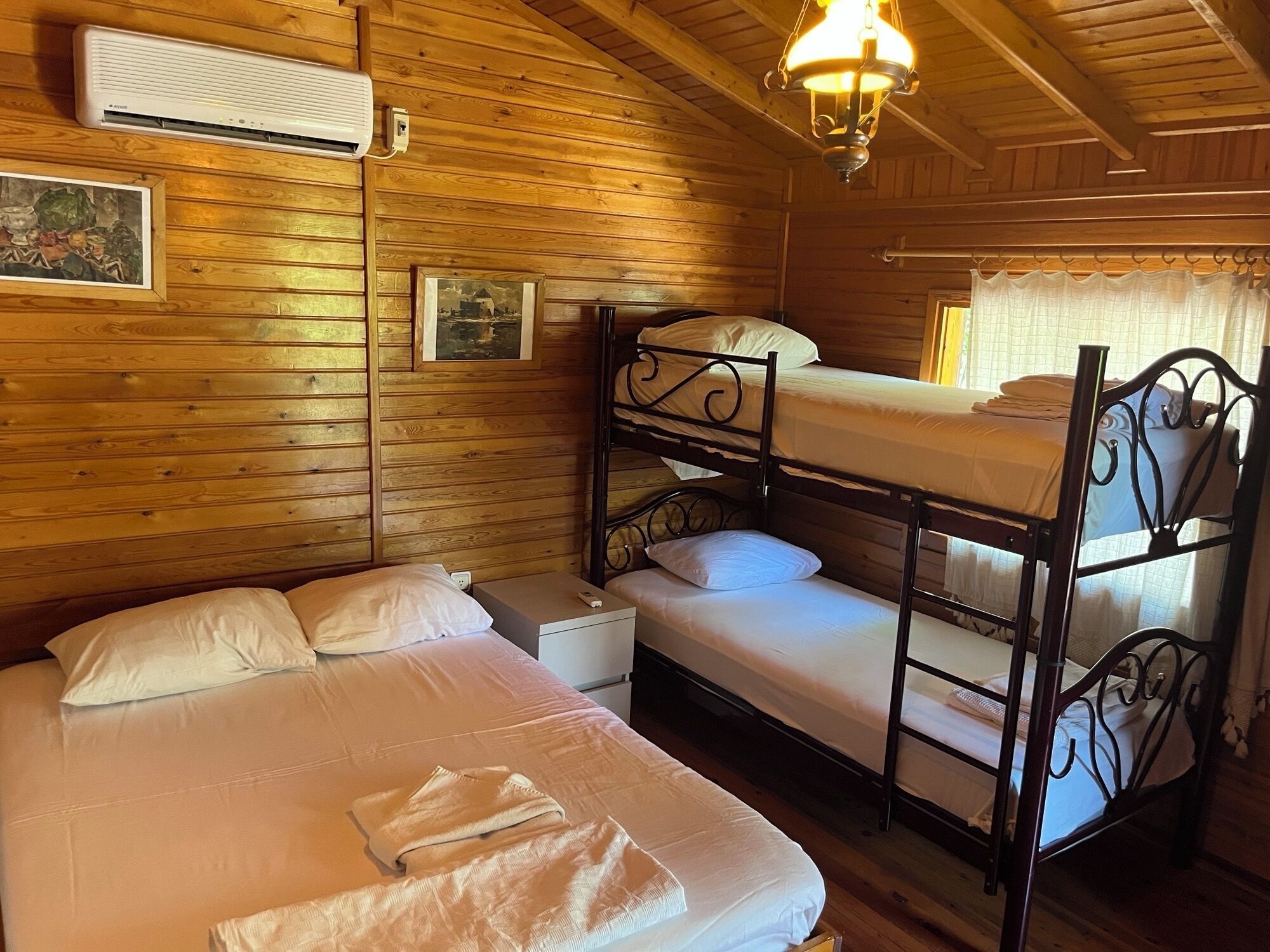 A wooden cabin room with bunk beds, a bedside table, and a hanging light fixture.
