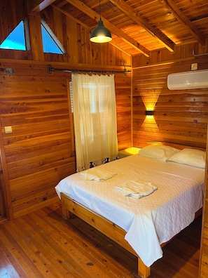 Un dormitorio de cabaña de madera con una cama, una lámpara colgante y una ventana con vistas.