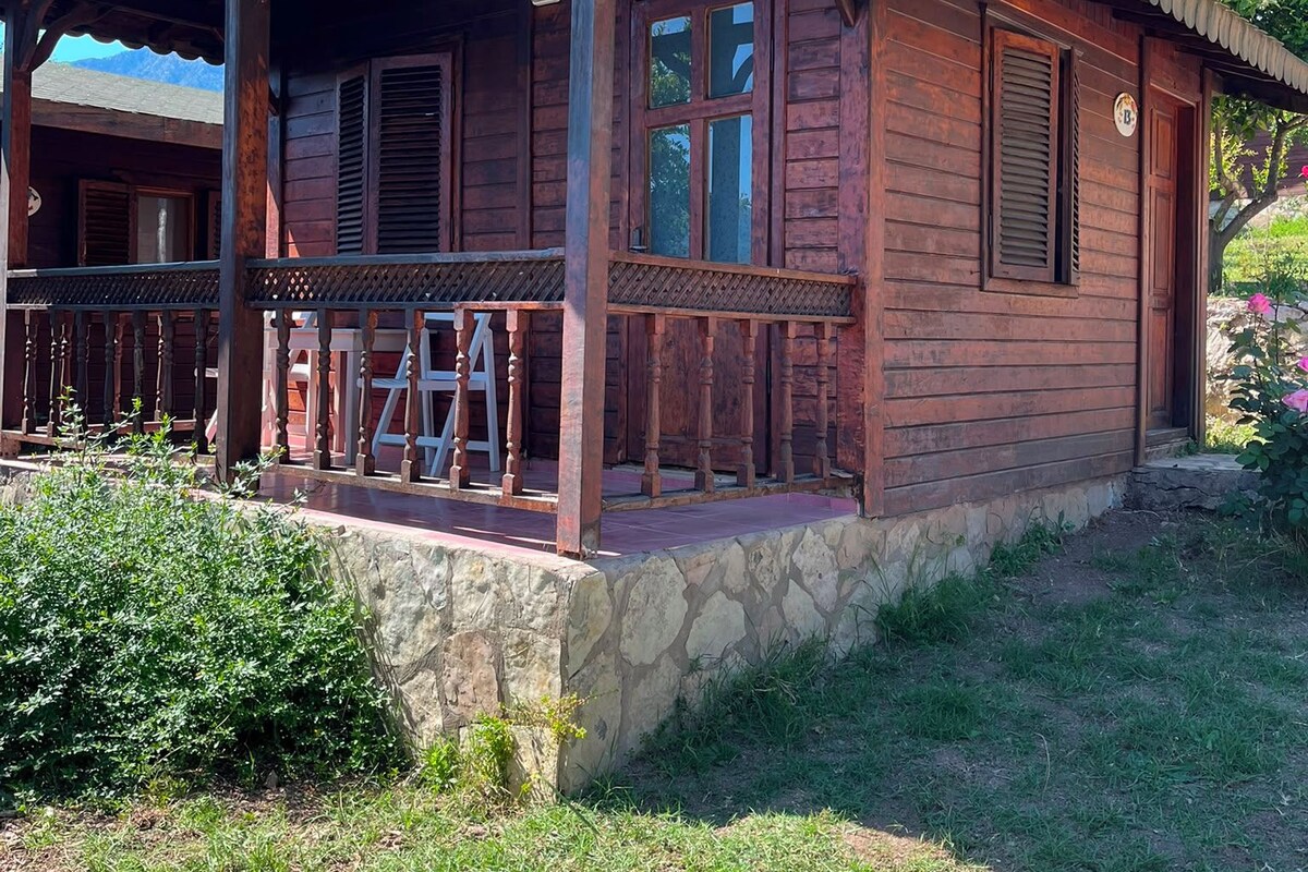 A wooden cabin with a porch, stone foundation, and a clear sky.
