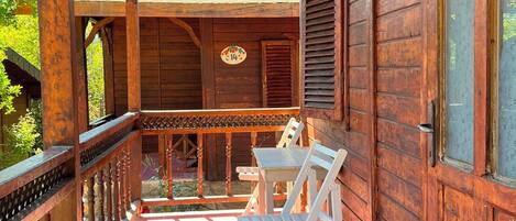 Un porche de madera con una mesa y sillas, una barandilla y vistas a un jardín.