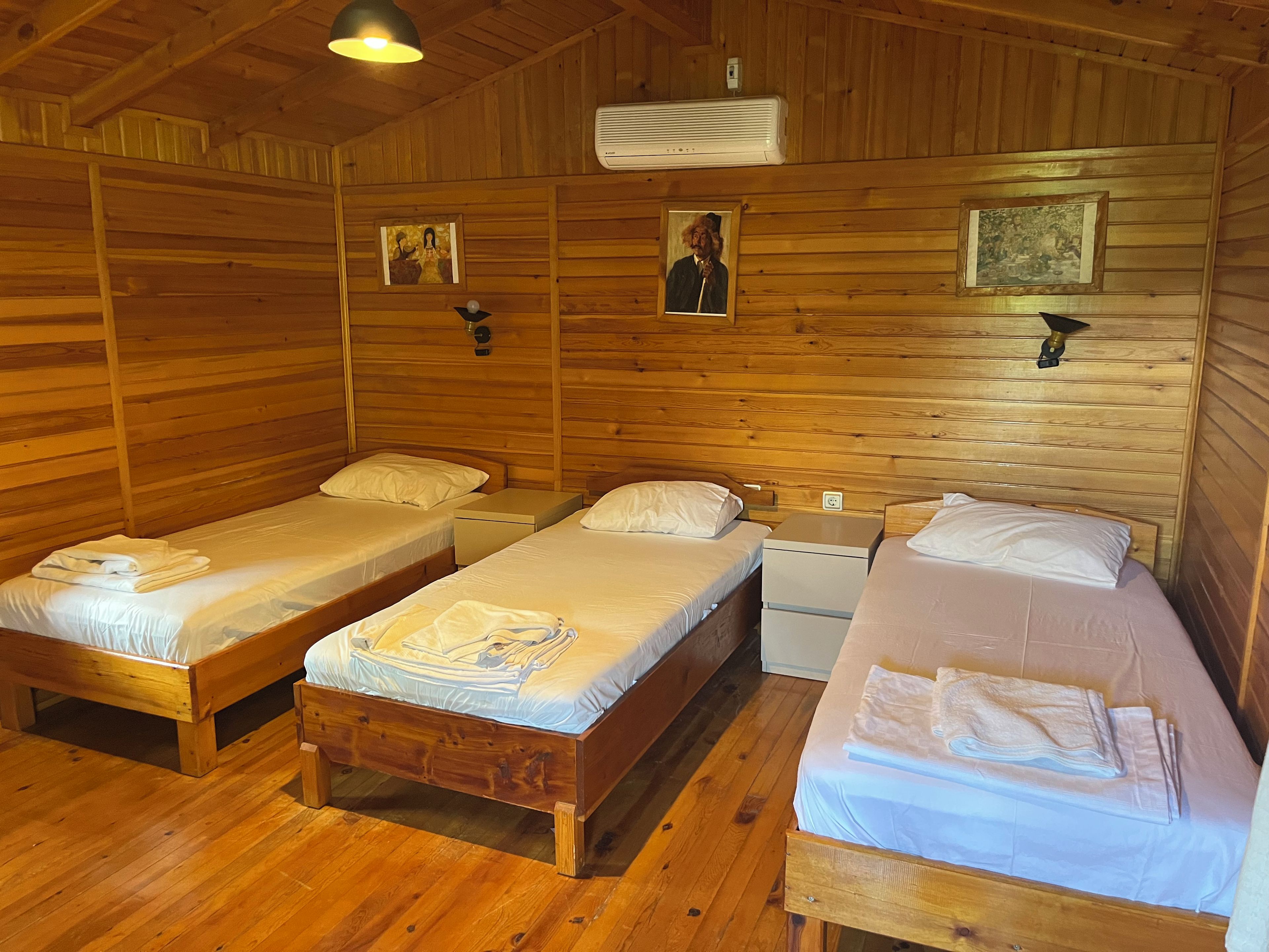 Una cabaña con tres camas de madera, cada una con una almohada y una toalla doblada. Hay luces fijadas en la pared y un ventilador de techo.