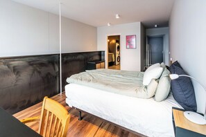 A bedroom with a bed, a desk, a chair, a washing machine, and a door leading to another room. - SIF Apartments Reykjavik - Two Floors 1 Bedroom (Reykjavík)