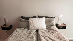 A bed with a striped comforter and multiple pillows, flanked by bedside tables with lamps. - SIF Apartments Reykjavik - Two Floors 1 Bedroom (Reykjavík)