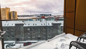 A snowy balcony with a view of a cityscape, including multi-story buildings and parked cars. - SIF Apartments Reykjavik - Two Floors 1 Bedroom (Reykjavík)