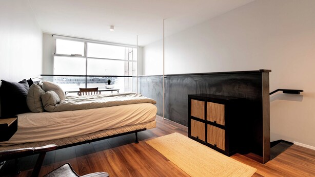 A modern bedroom with a bed, a small table, and a view of the city through large windows. - SIF Apartments Reykjavik - Two Floors 1 Bedroom (Reykjavík)