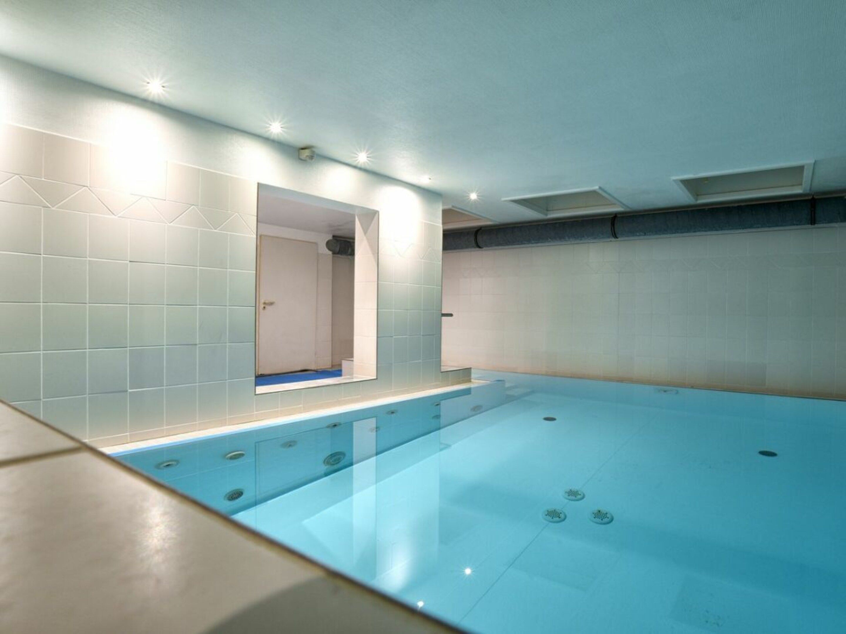 A swimming pool with a glass enclosure, a tiled wall, and a door leading to a shower area.